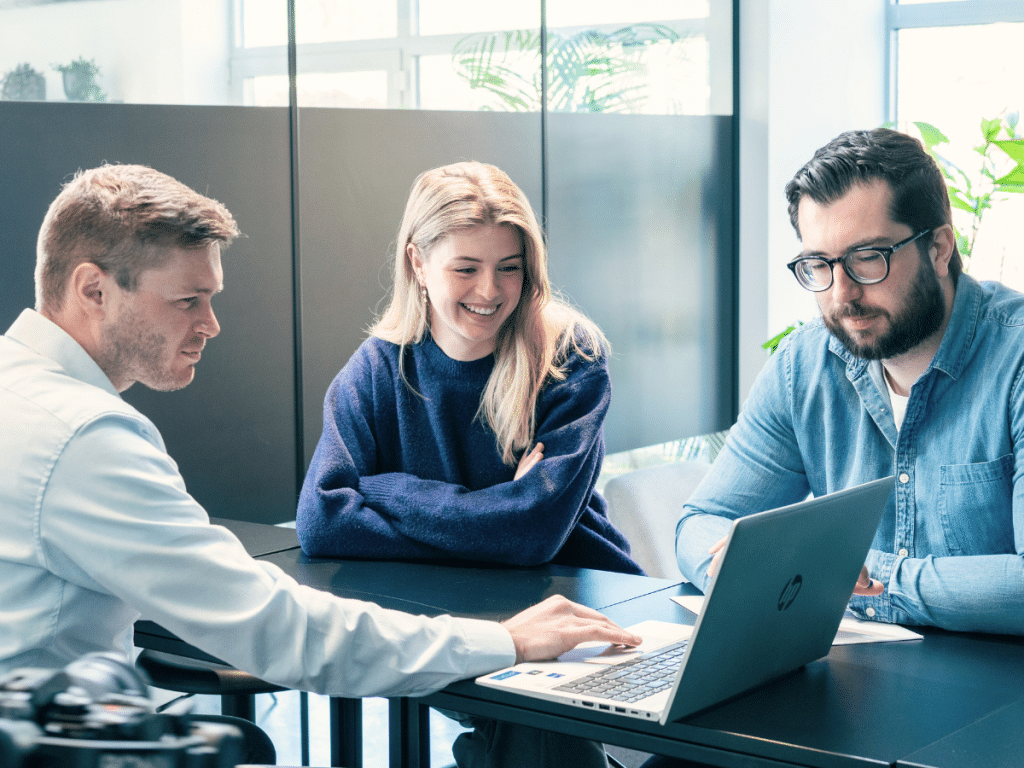 Jens, Layla en Maxime bespreken campagnes en resultaten rond een laptop in vergaderruimte.